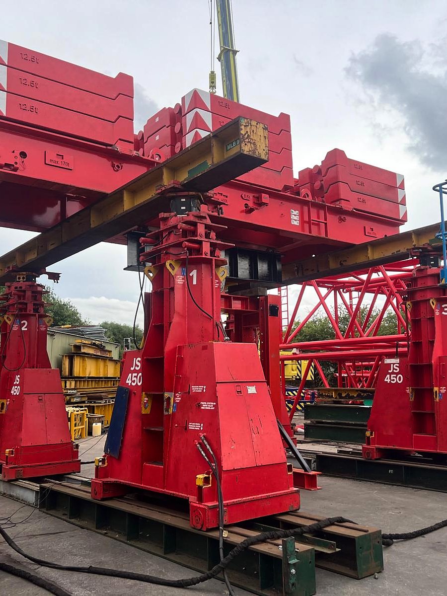 Red heavy lifting towers holding a steel beam, on site