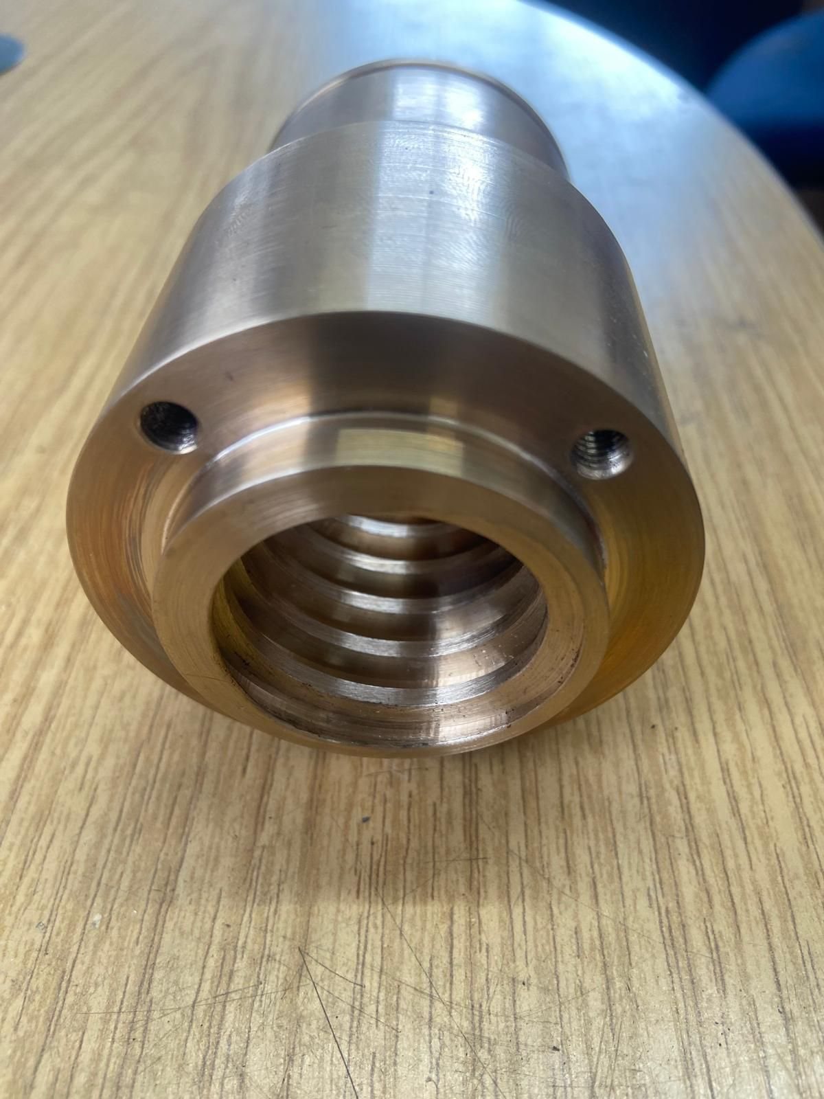 A machined nut with an internal thread and two holes in its face, on the bench
