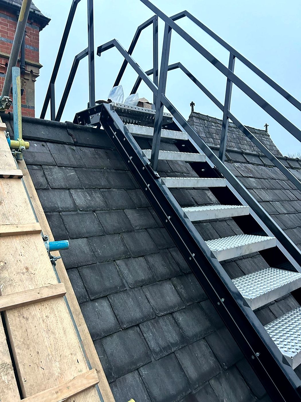 A black steel access staircase with handrails fixed up a slate roof