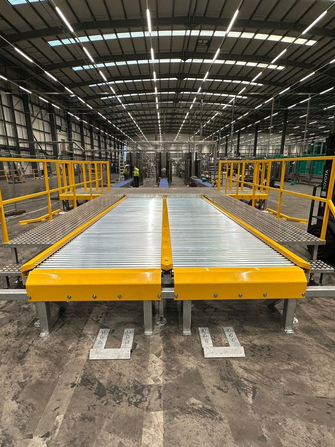 Twin roller bed conveyors with yellow guard rails running down a long warehouse