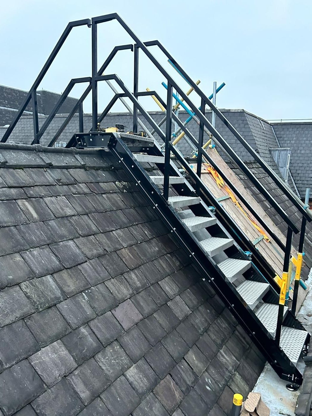 A black steel access staircase with handrails going up and over a slate roof