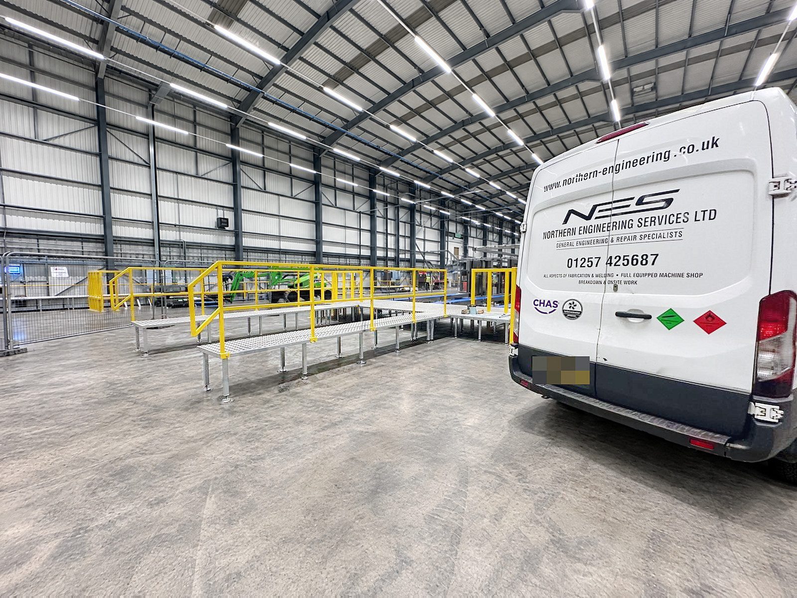 Low galvanised walkways with yellow handrails inside a large warehouse, the NES van parked on the right