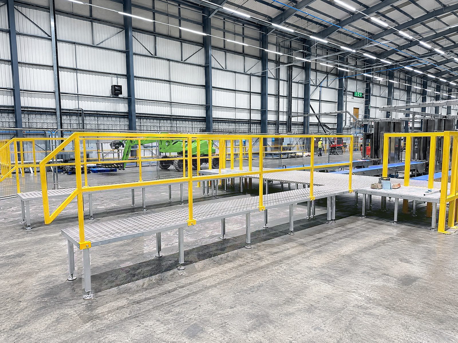 A long galvanised walkway with yellow handrails and a gate across a warehouse floor