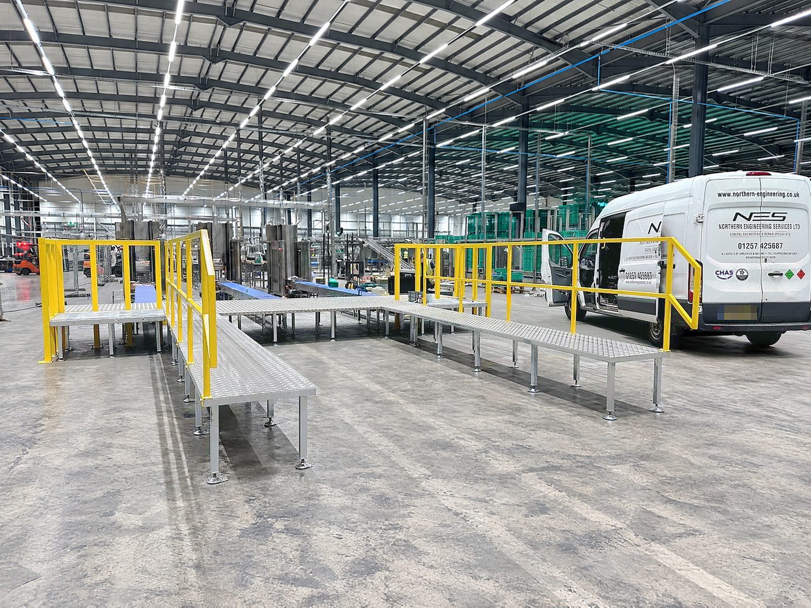 Galvanised walkways with yellow handrails running into a production area, the NES van alongside with its doors open