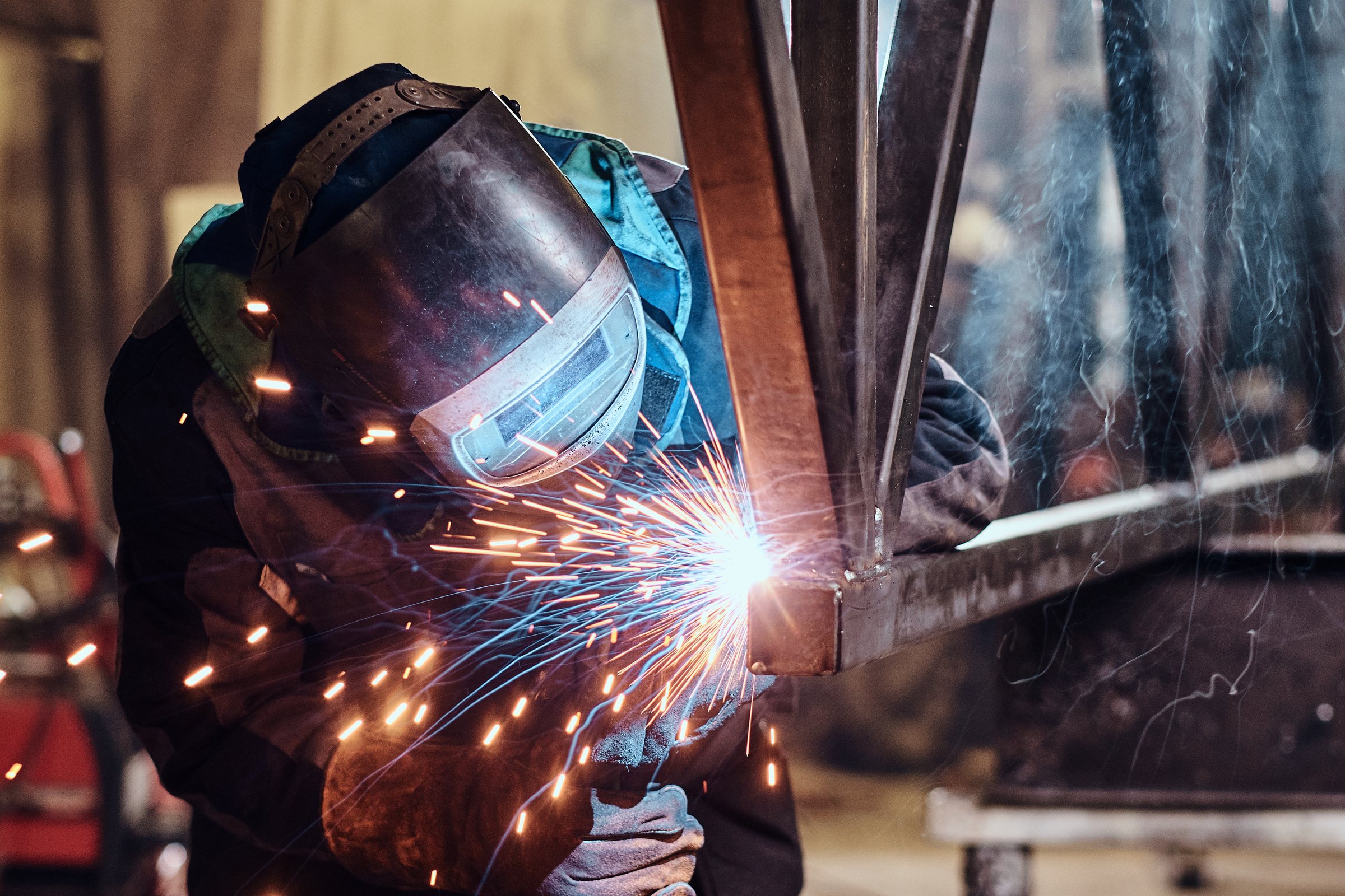 A welder in a mask welding a steel frame, sparks flying from the arc