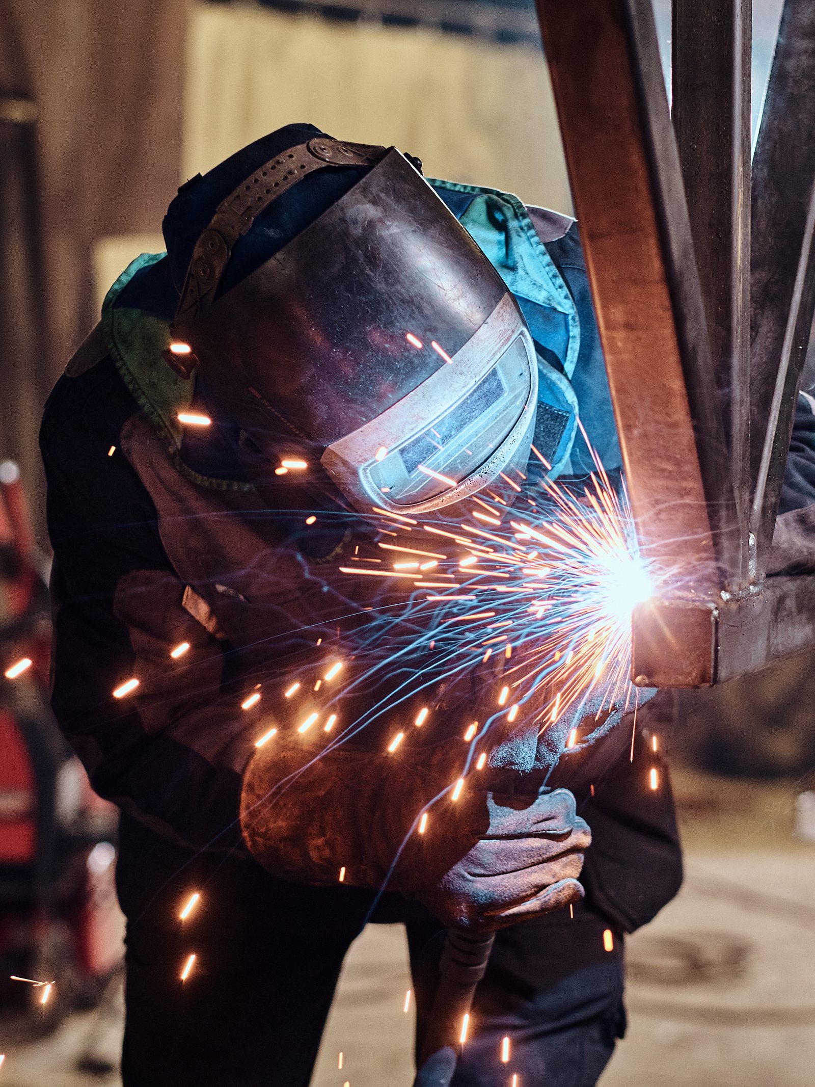 A welder in a mask welding a steel frame, sparks flying from the arc