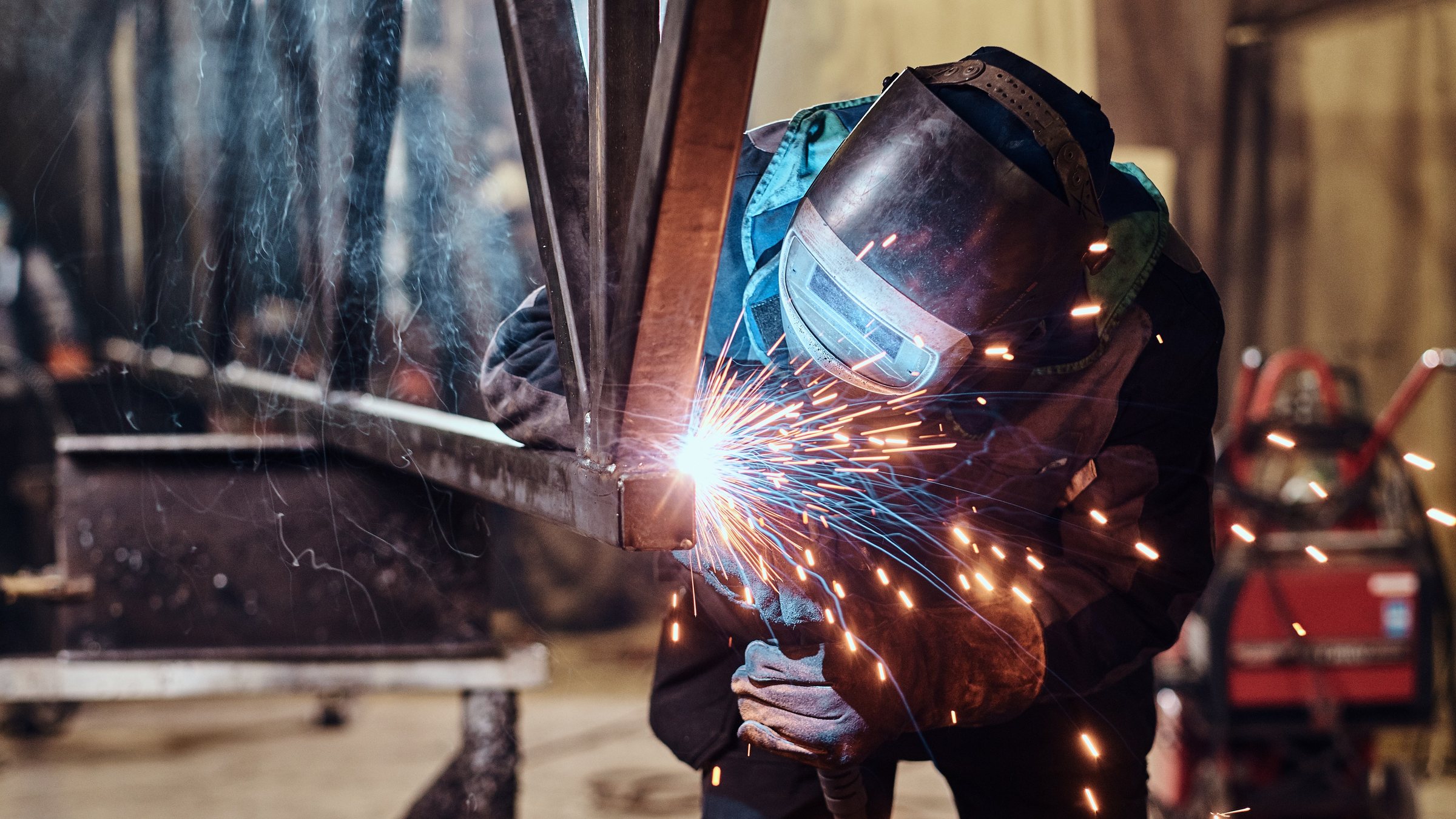 A welder in a mask welding a steel frame, sparks flying from the arc