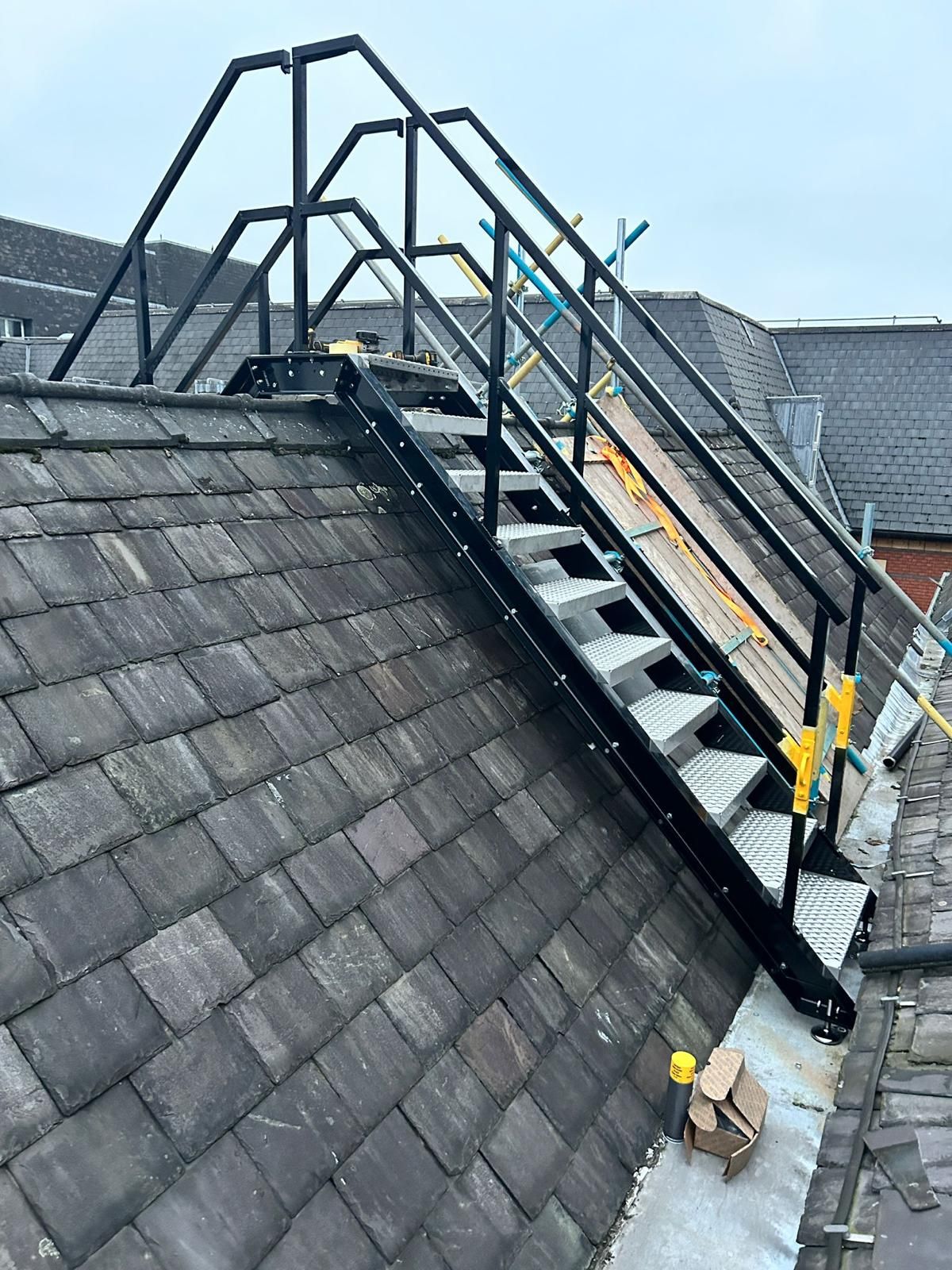 A black steel access staircase with handrails going up a slate roof